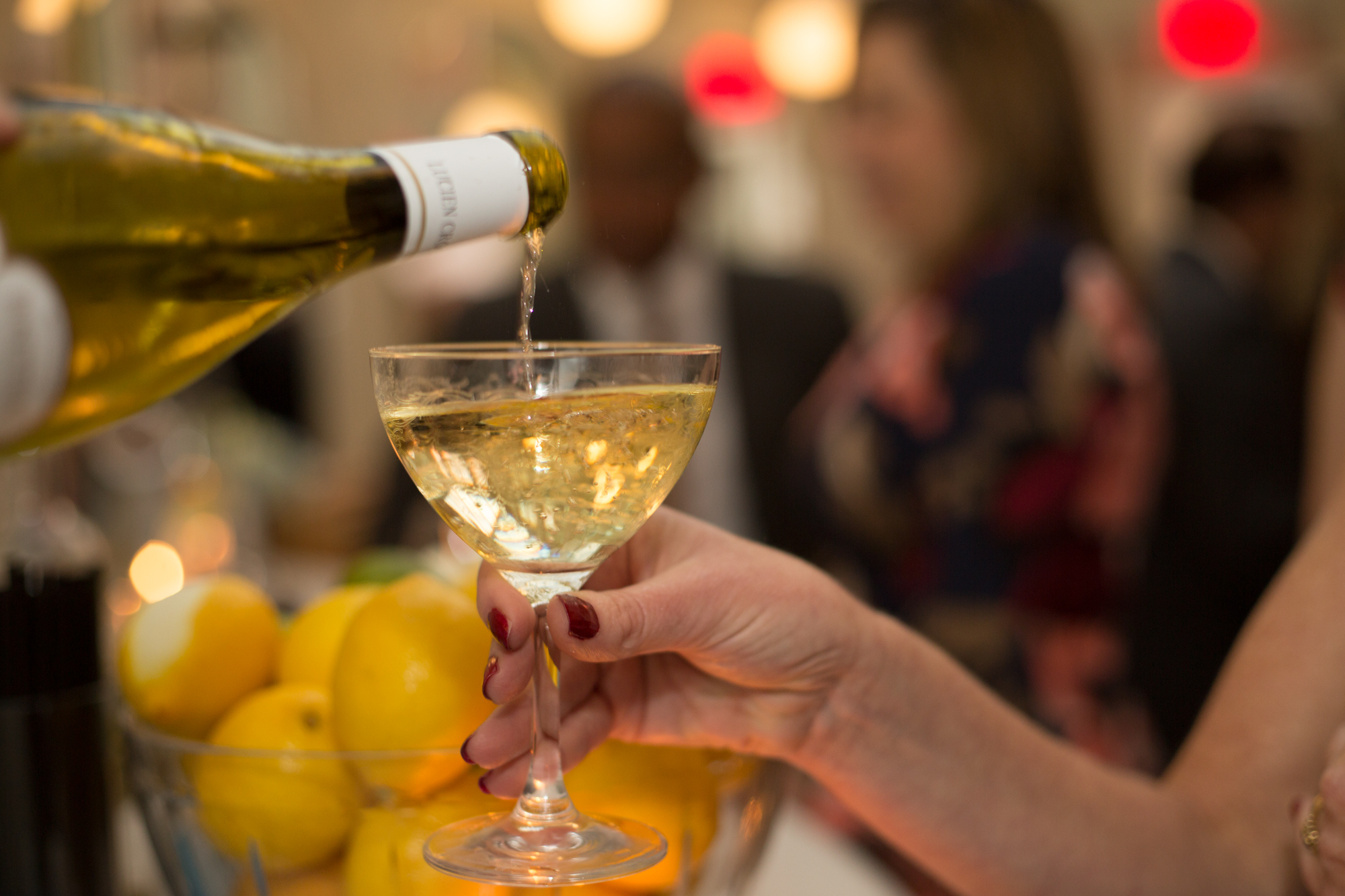bottle of champagne being poured into a champagne coupe glass that is being held by a female guest.