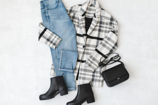 Blue jeans, striped coat, small black cross body bag and leather ankle boots on grey background. Overhead view of woman's casual day outfits. Trendy hipster look. Flat lay.