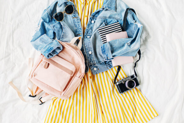 Blue jean jacket and Yellow dress  with backpack, book and photo camera on white. Women's stylish autumn or spring outfit. Trendy clothes for college. Back to school concept.  Flat lay, top view.